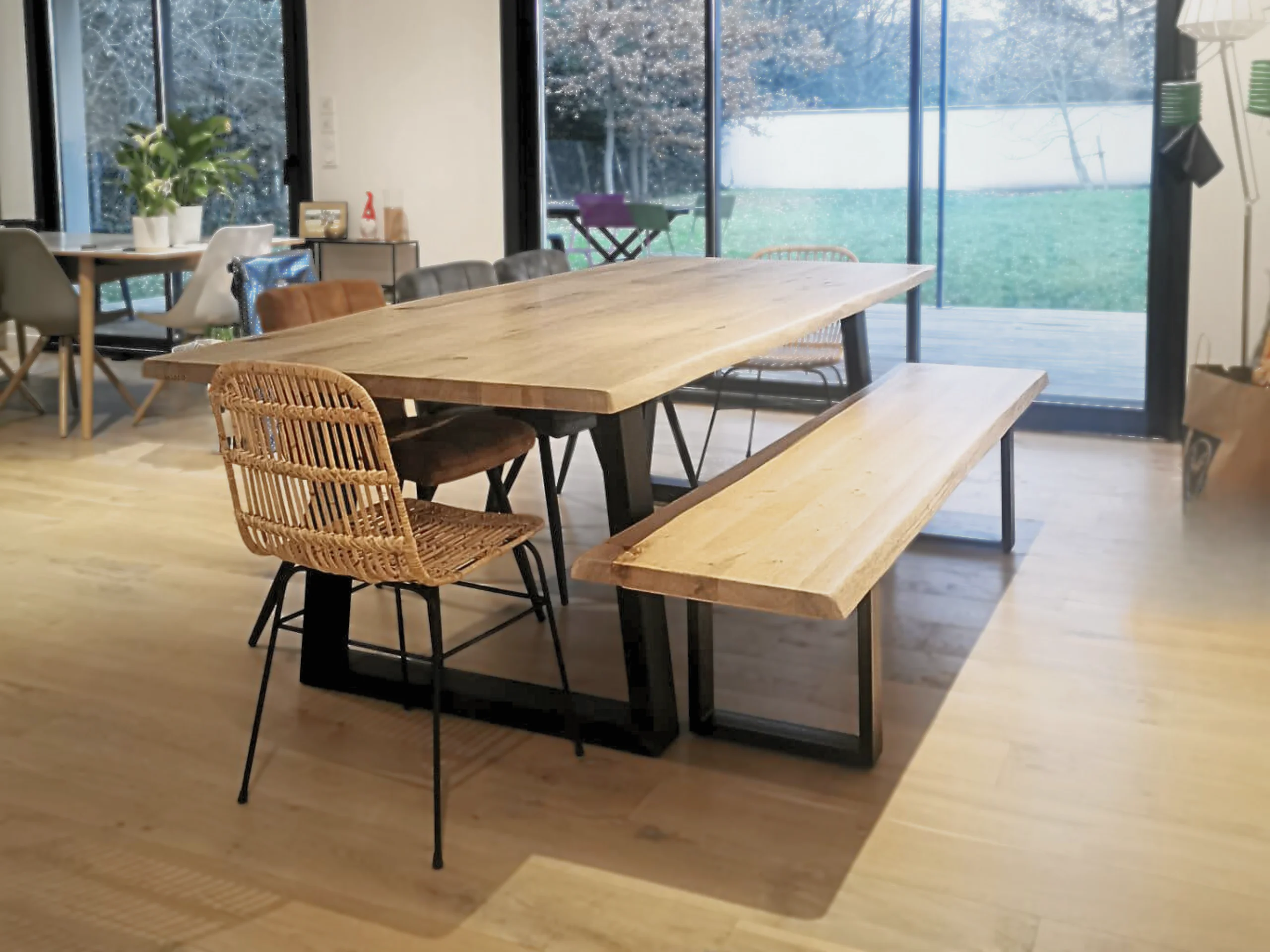 Un salon avec une table doté de pied en acier en forme de trapèze, un banc avec des pieds en U et une chaise en roti