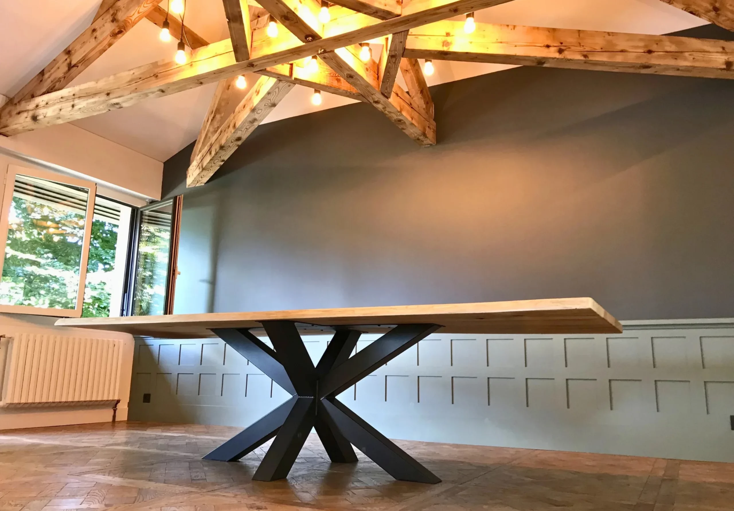 A large living room with a solid wood table, with a sturdy steel central star base